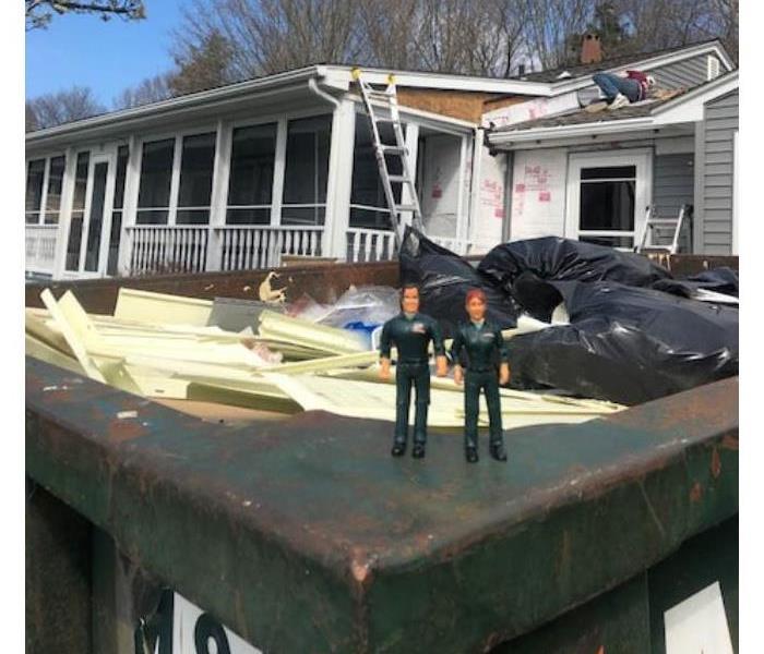 two action figures on a trash bin in front of a home