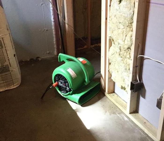 a green air mover in a basement with sheetrock cut from the bottom half of the wall 